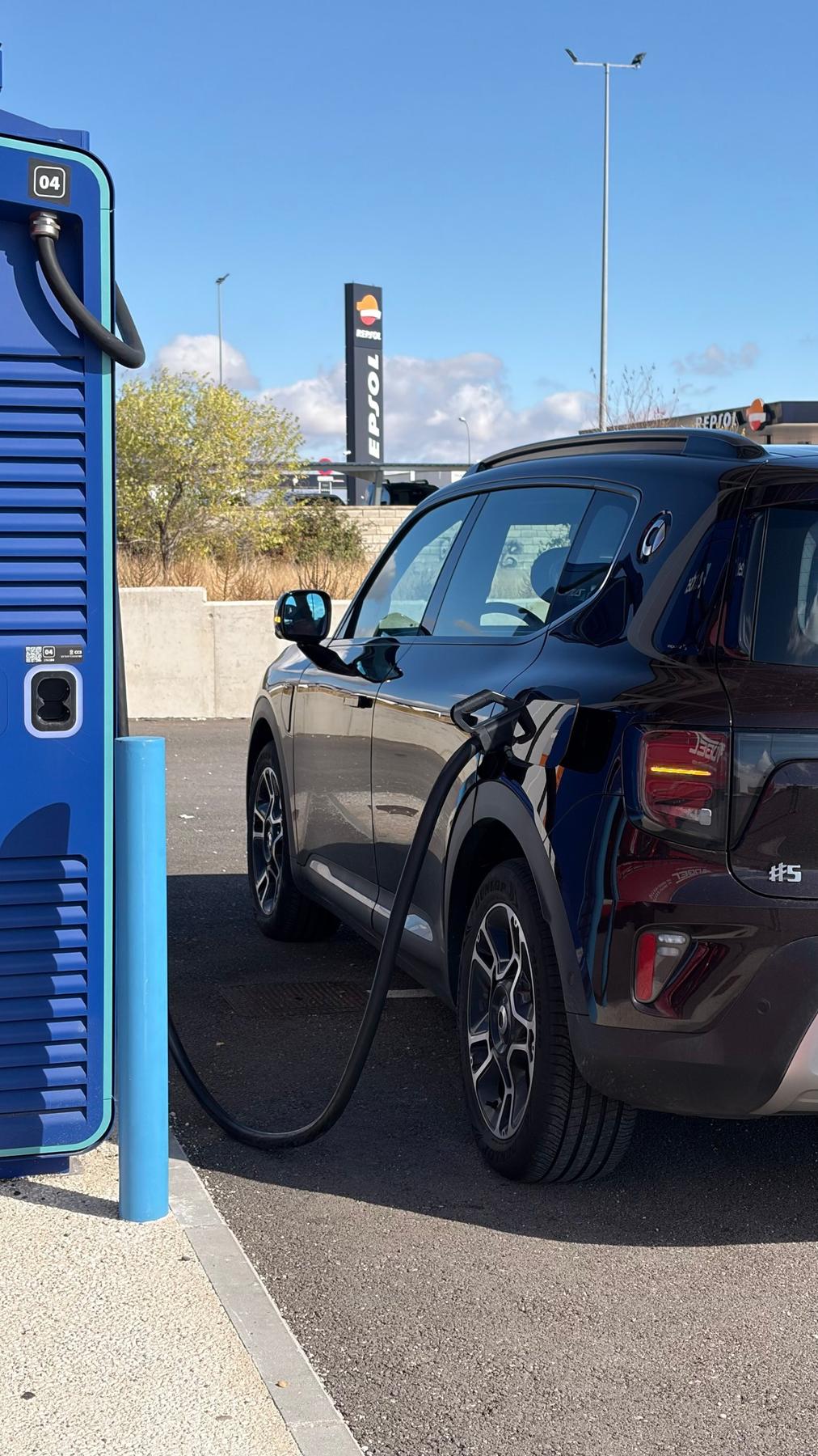 smart #5 Pro+ cargando en un cargador rápido azul junto a una estación de servicio Repsol, con el cable enchufado en el lateral trasero