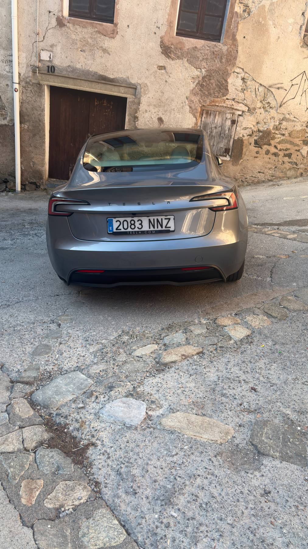 Trasera del Tesla Model 3 gris aparcado en una calle empedrada de Setcases, frente a una fachada de piedra